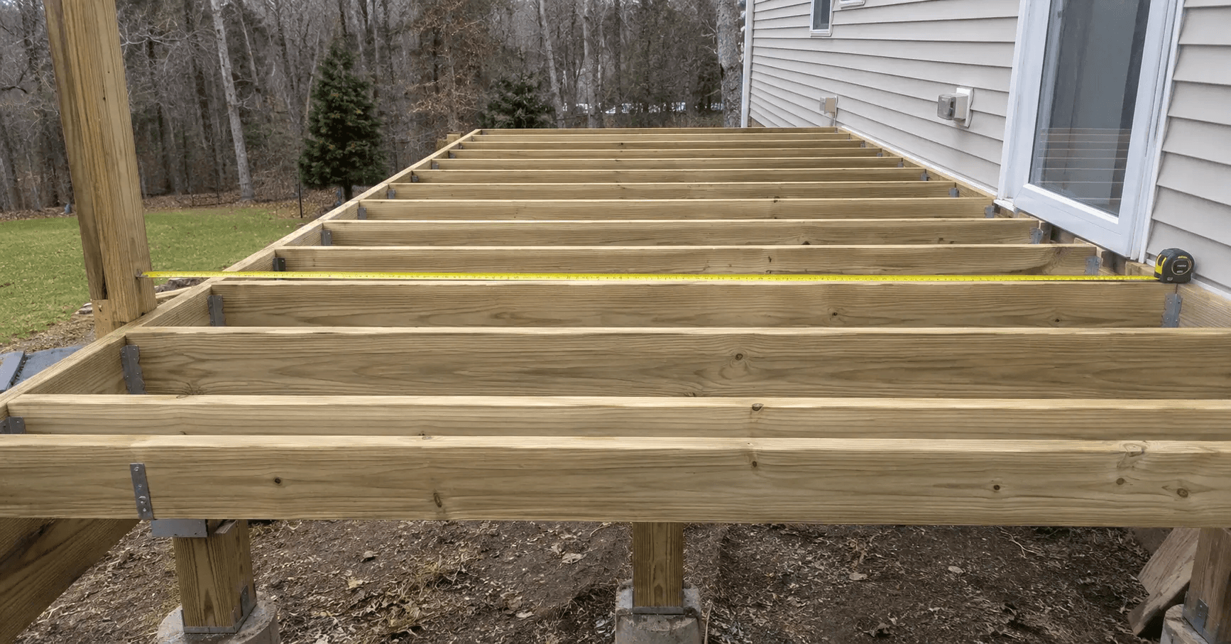 Open deck frame with joists in hangers before decking is installed, tape measure across joist spacing